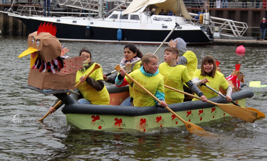 Kinder sitzen paddelnd in einem Pappboot.