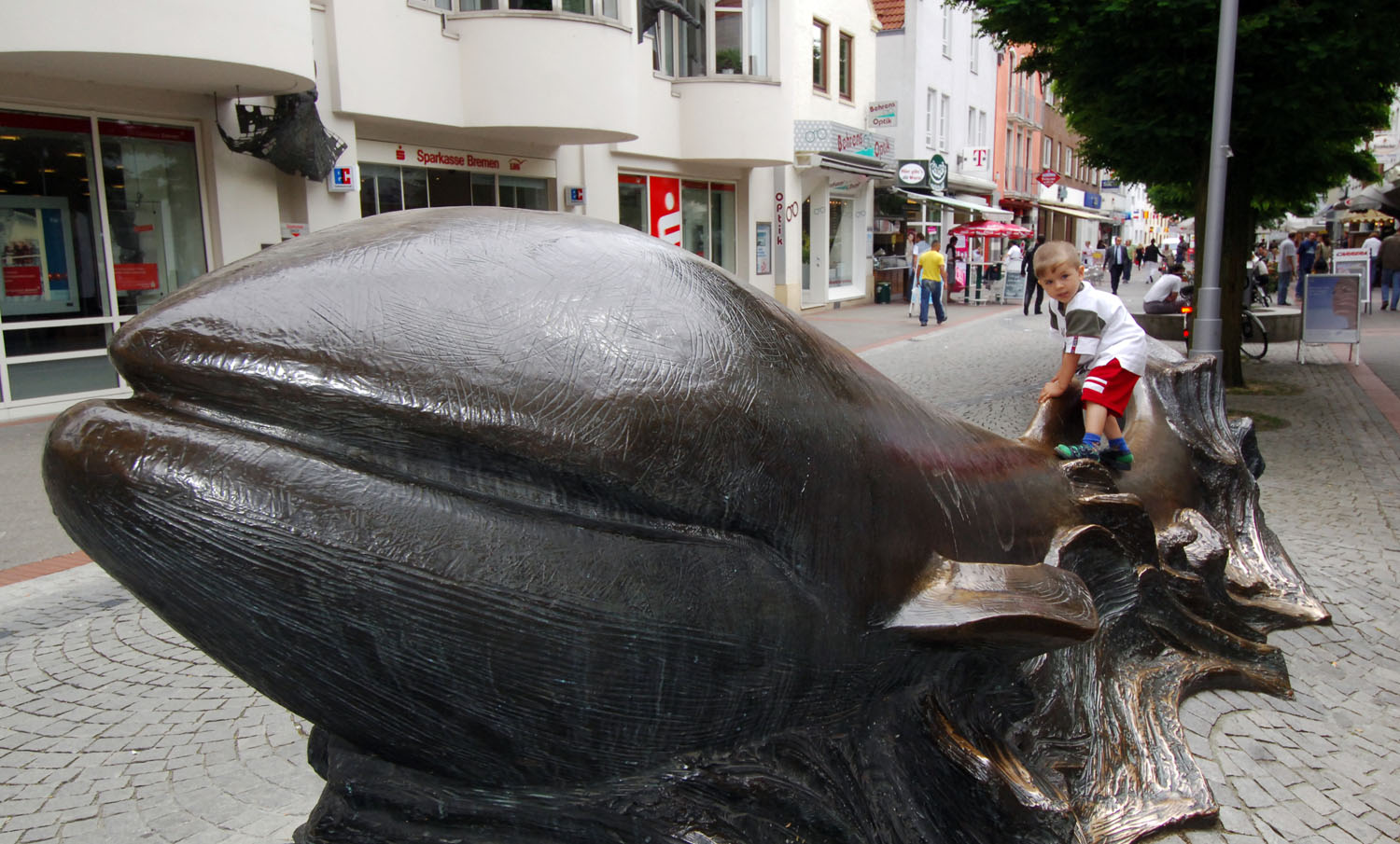 Ein großer Bronzewal steht in der Vegesacker Innenstadt. Ein Junge klettert daran.