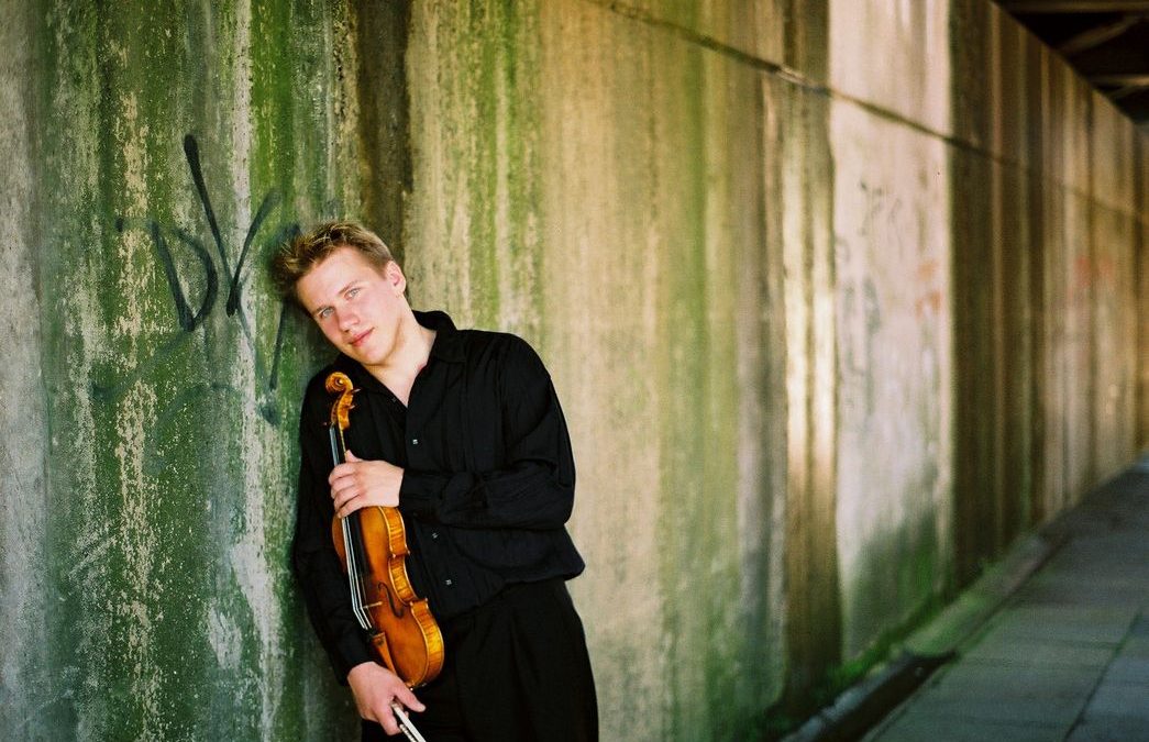 Junger Mann lehnt sich mit einer Violine an die Wand