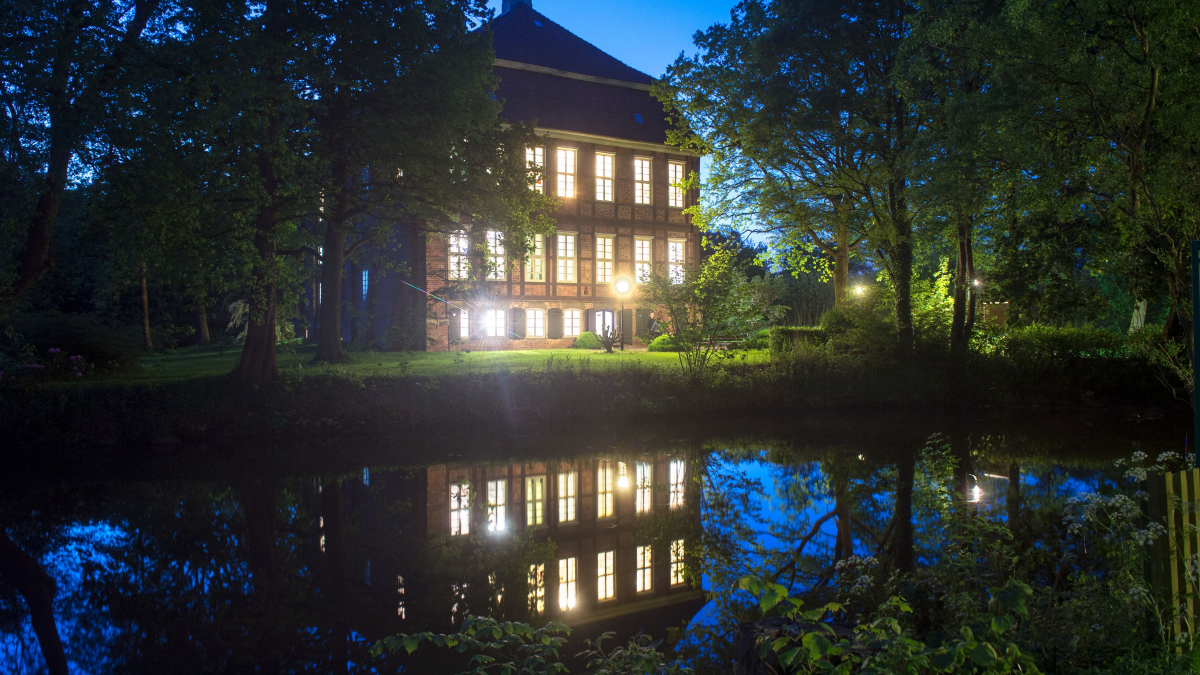 Nachtaufnahme vom Schloss Schönebeck. Die Lichter des Schlosses spiegeln sich im Wasser.