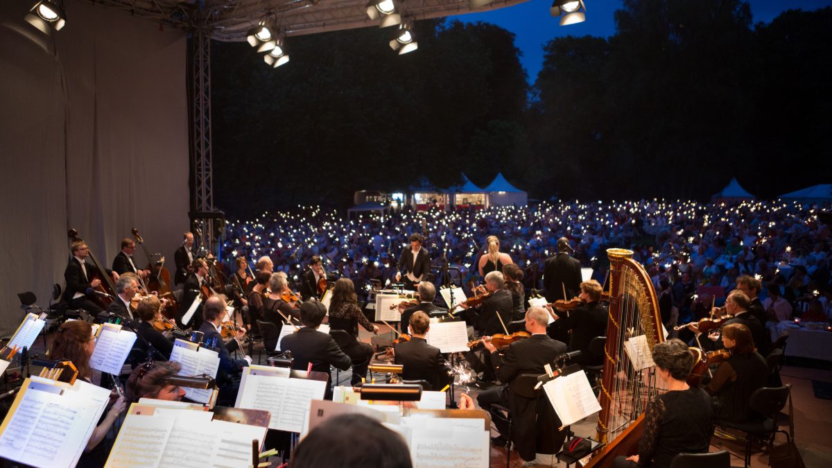 Publikum sitzt vor einer Bühne mit einem Orchester