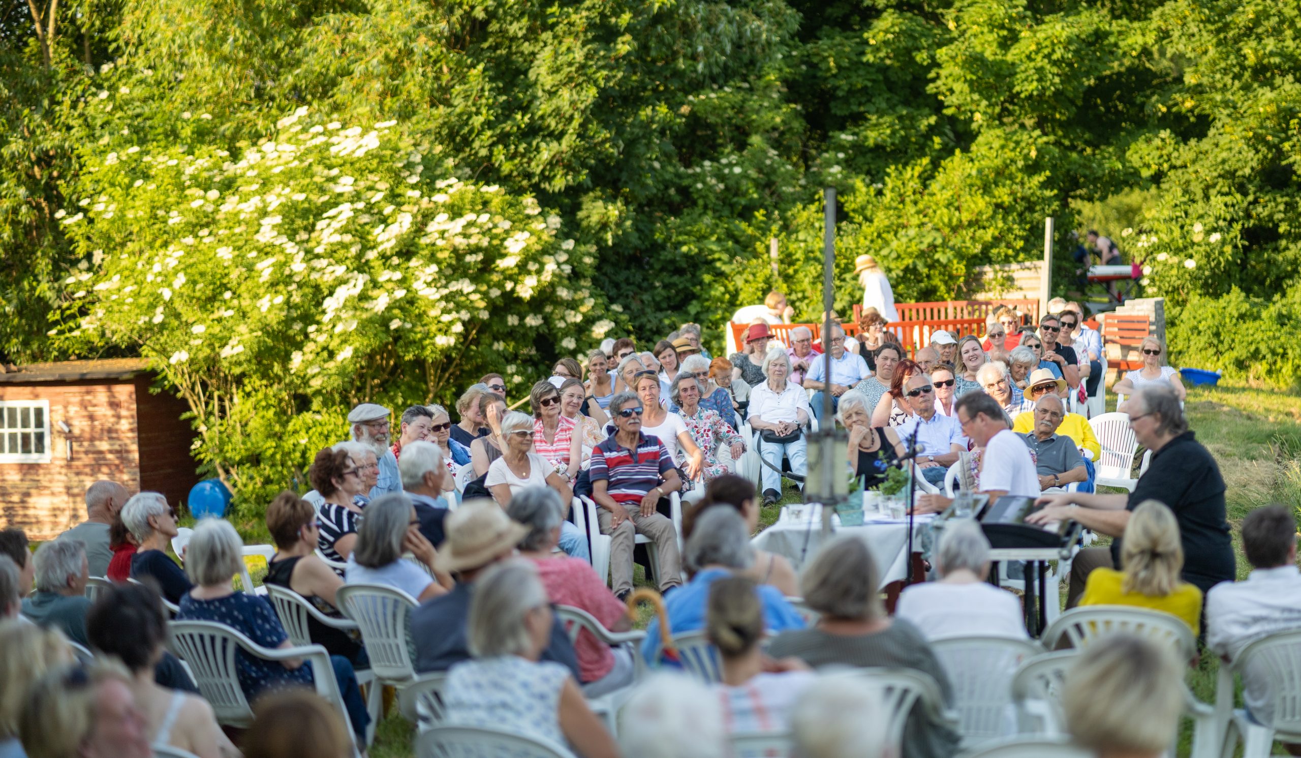 Viele Menschen sitzen im Grünen und hören Musikern zu.