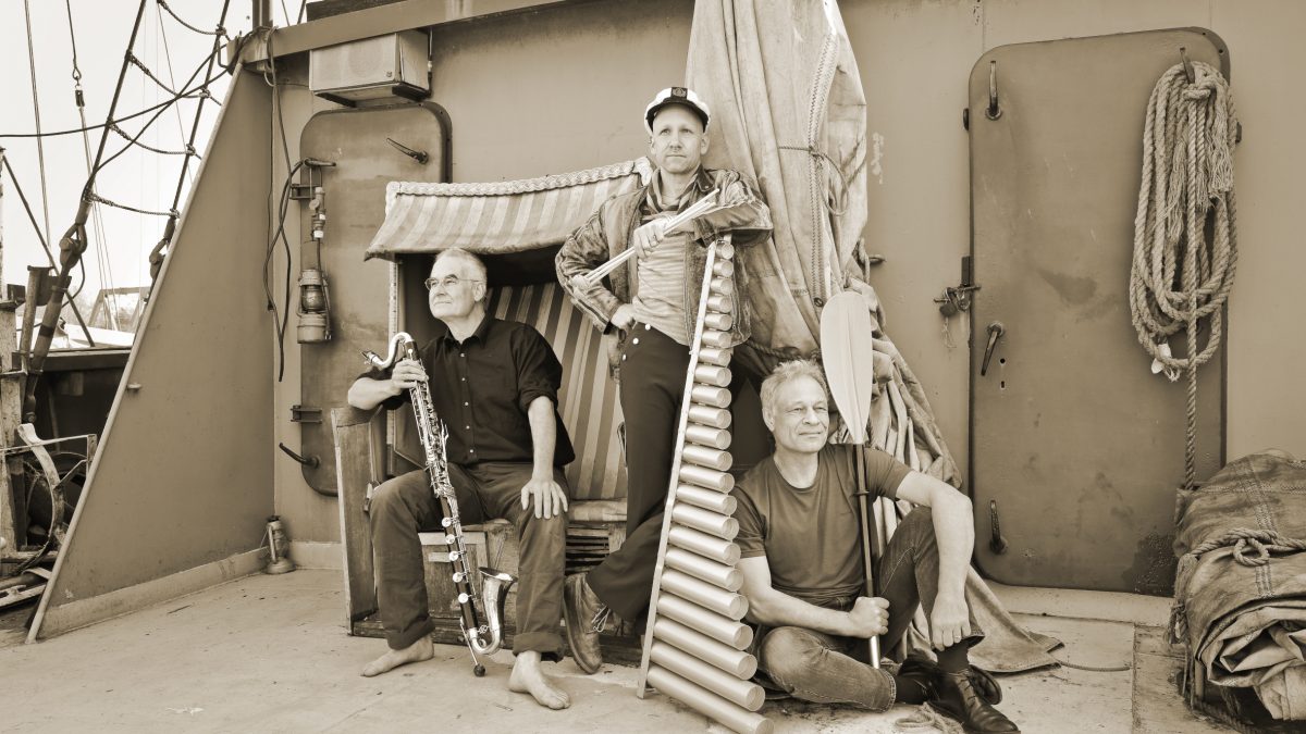 Drei Männer mit ihren Musikinstrumenten sitzen auf einem Schiffsdeck