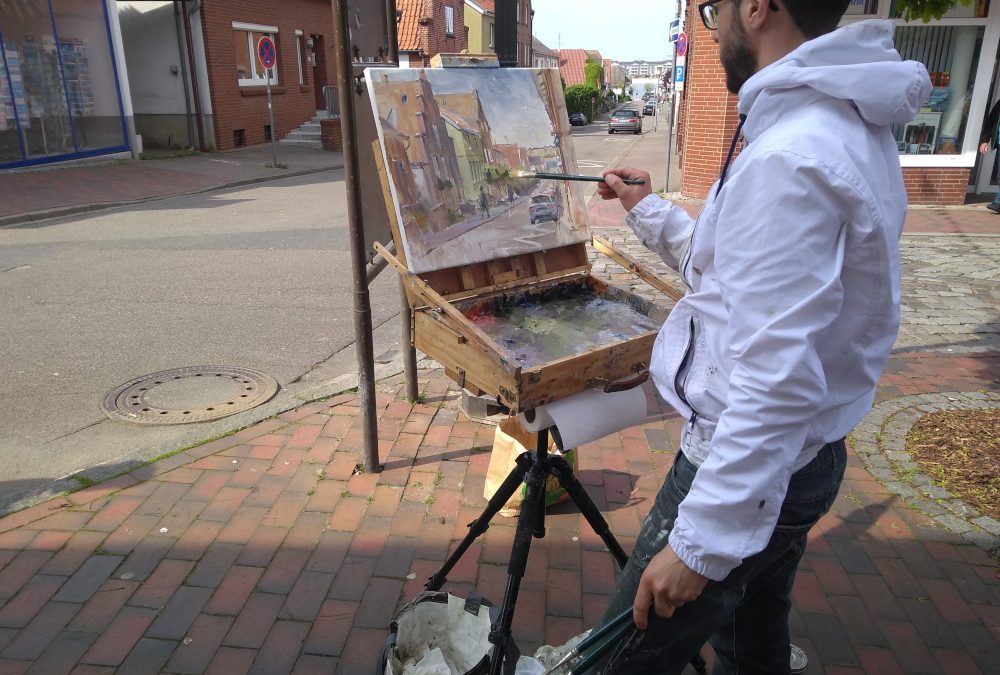 Ein Mann steht in einer Straße und malt auf einem Stativ