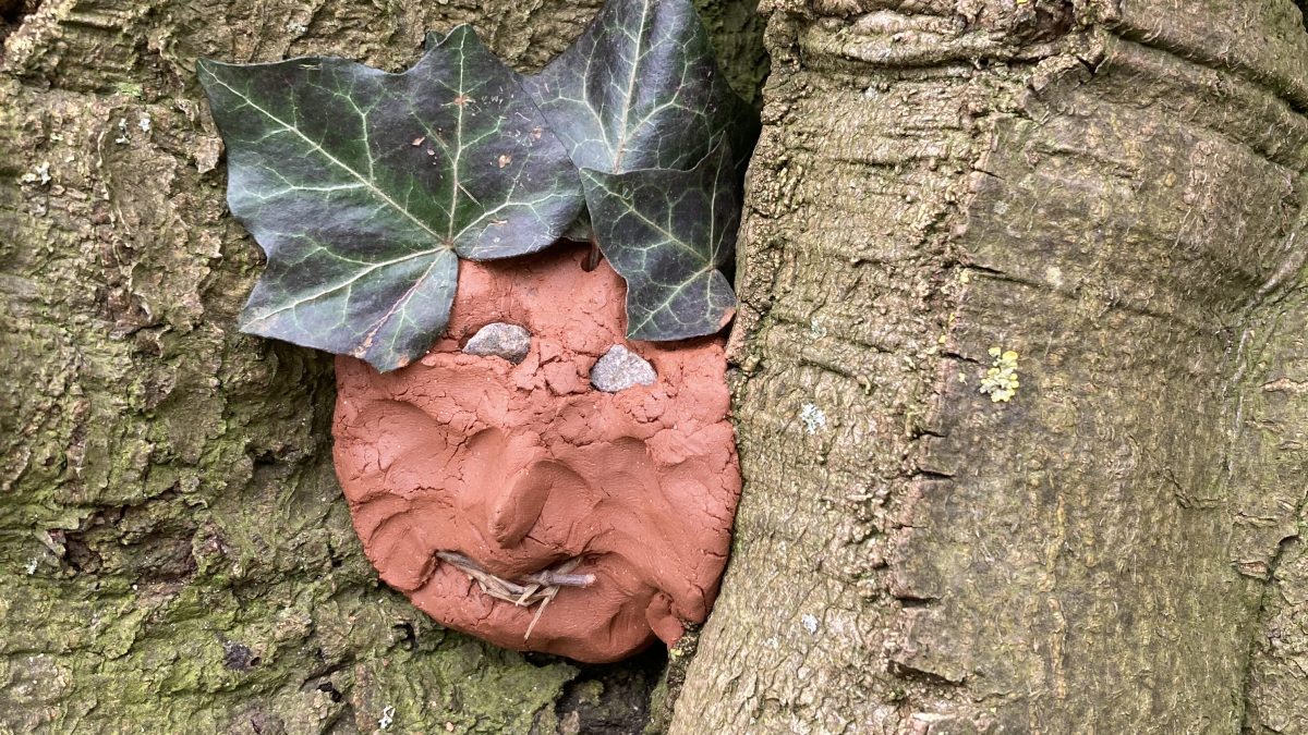 Ein selbstgebasteltes Gesicht au gebranntem Ton liegt zwischen Ästen auf einem Baum
