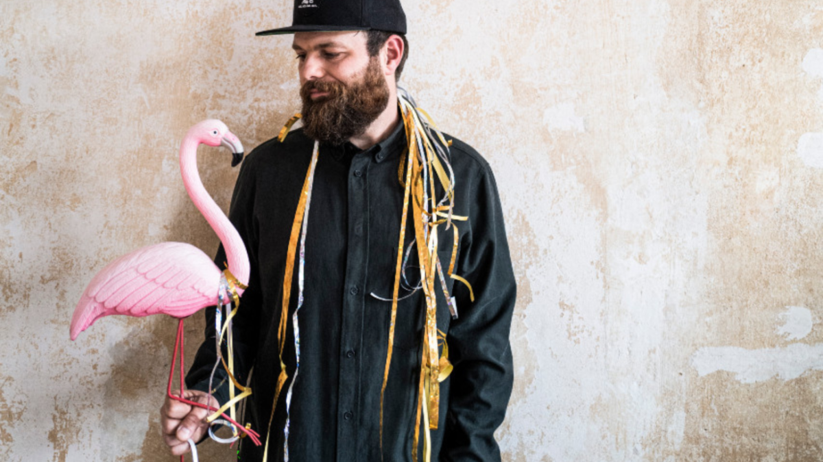 Ein Mann hat bunte Girlanden um den Hals und einen Flamingo aus Plastik in der Hand