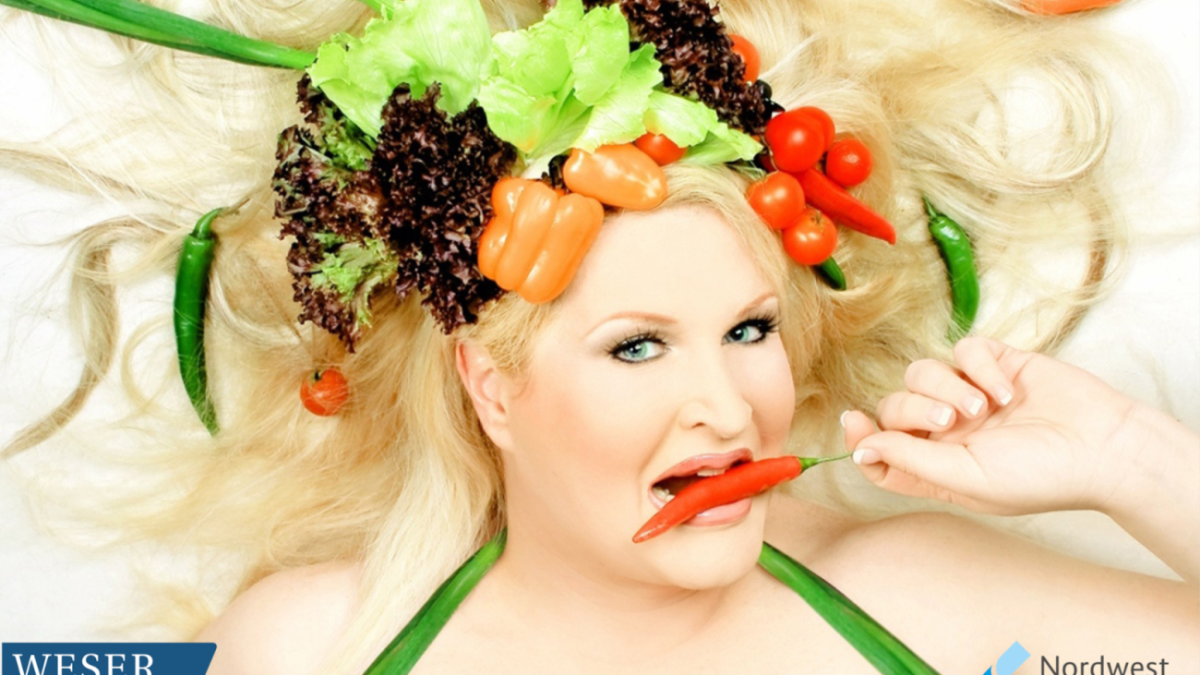 Eine Frau mit Gemüse auf den Kopf und einer Chili im Mund.