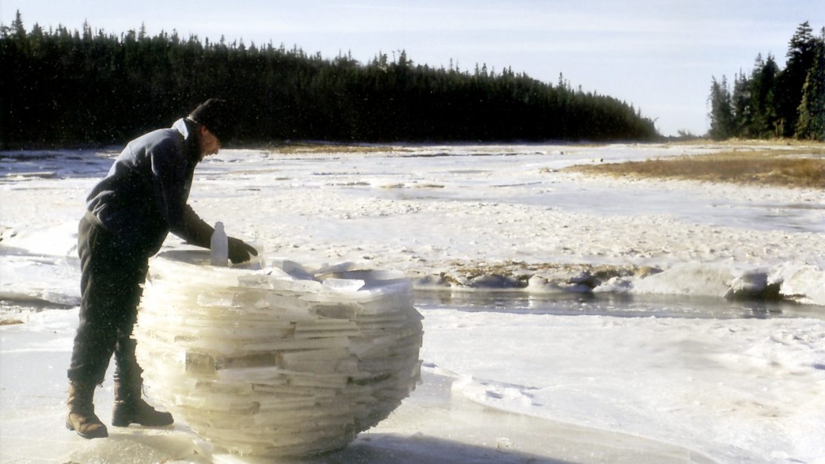 Ein Mann steht auf einem zugefroreren Fluss und baut eine Skulptur aus Eisblöcken