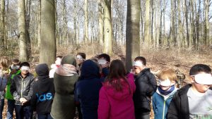 Kinder stehen aufgereiht im Wald und haben Masken auf den Augen