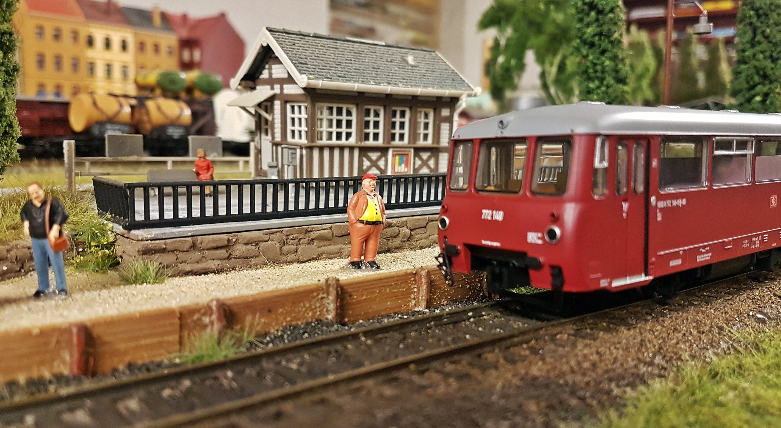 Miniatureisenbahnlandschaft. Ein Mann steht an einem Bahngleis und artet auf den einfahrenden Zug