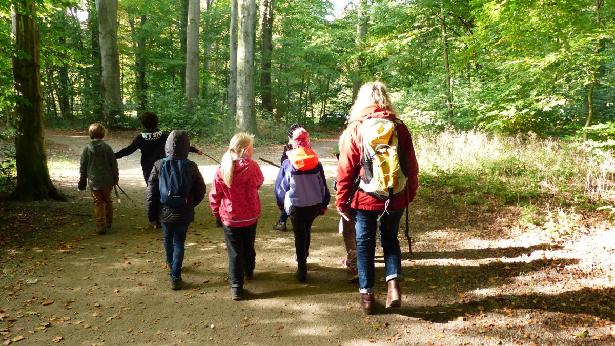 Kinder, begleitet von einer erwachsenen Frau, laufen durch einen Wald